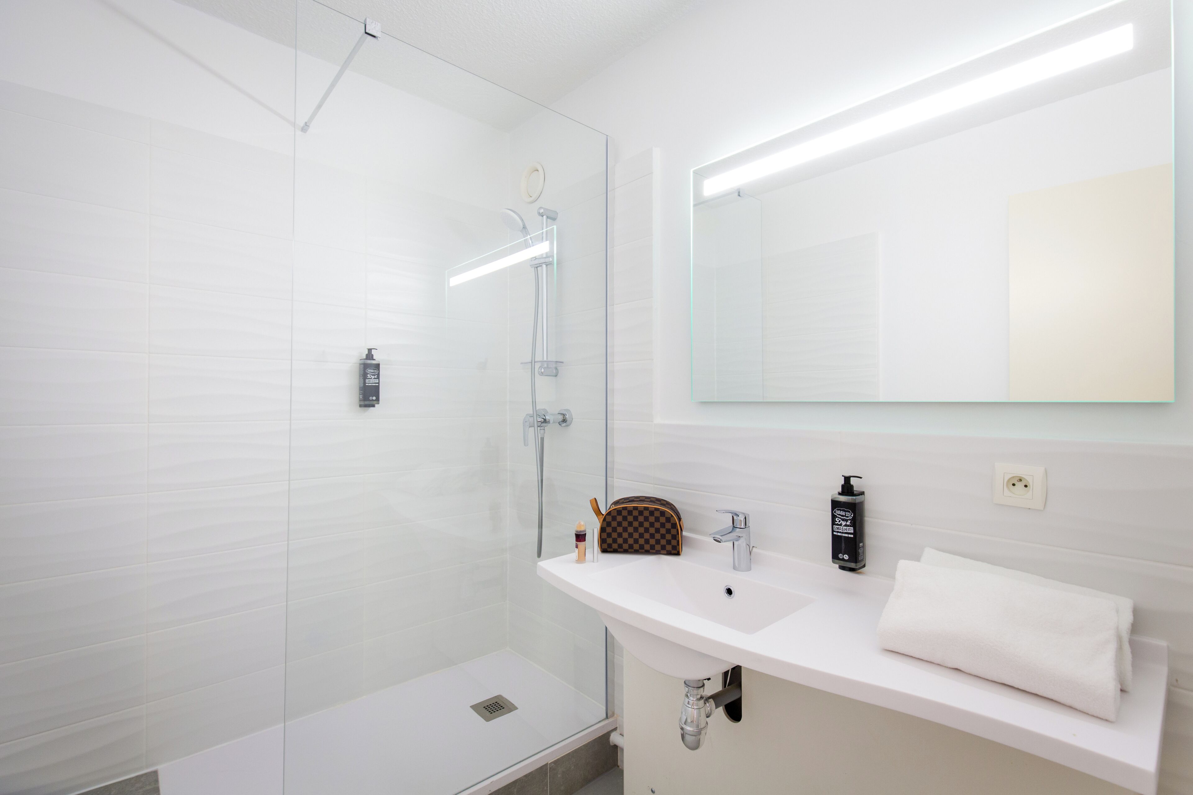 A modern bathroom with a glass shower enclosure, a white sink, a mirror, and a towel on the counter.