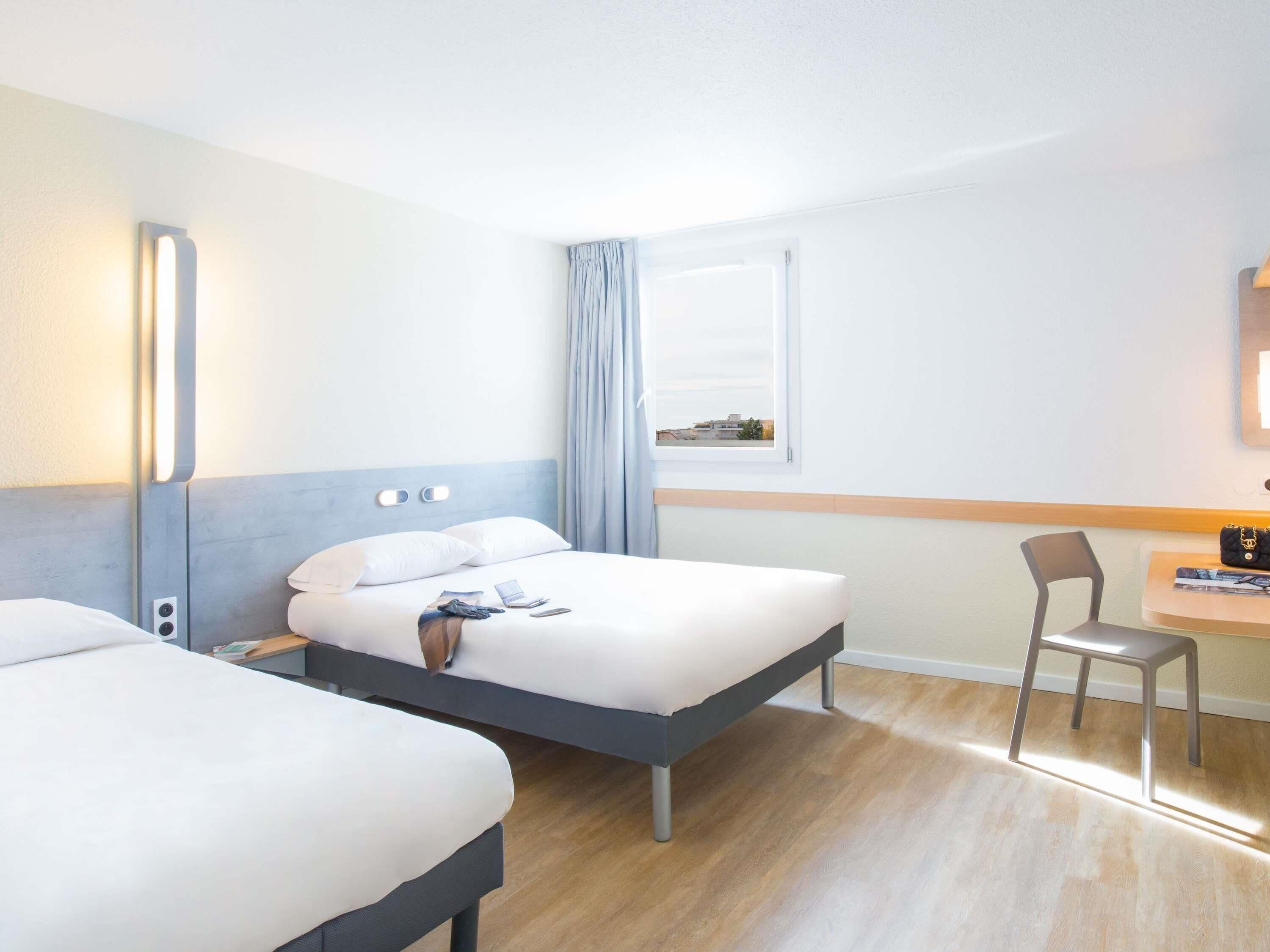 Ein Hotelzimmer mit zwei Betten, einem Schreibtisch, einem Stuhl und einem Vorhangfenster.