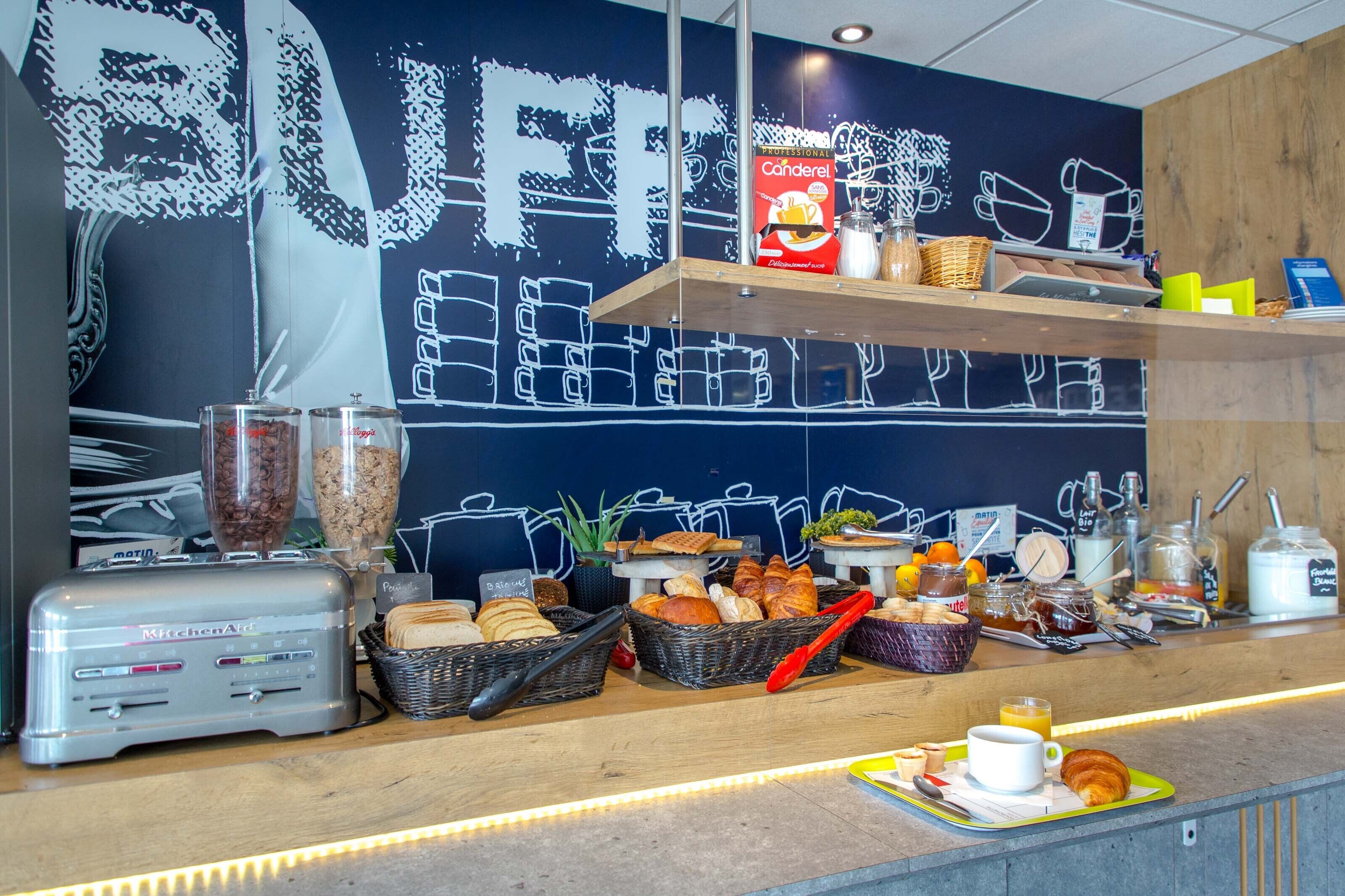A breakfast buffet with various food items, a coffee machine, and a wall with a coffee cup mural.