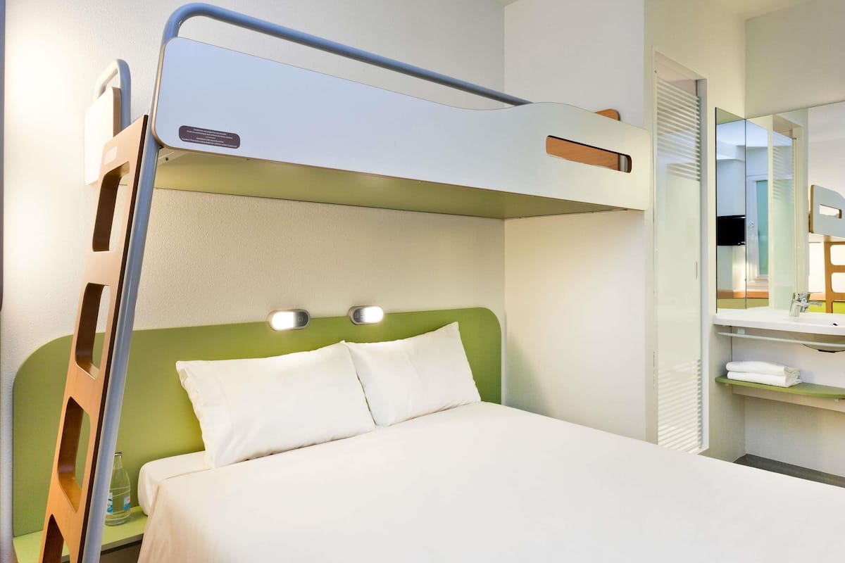 Un lit superposé avec une tête de lit verte, une table de chevet avec une lampe et un miroir au-dessus du lit.