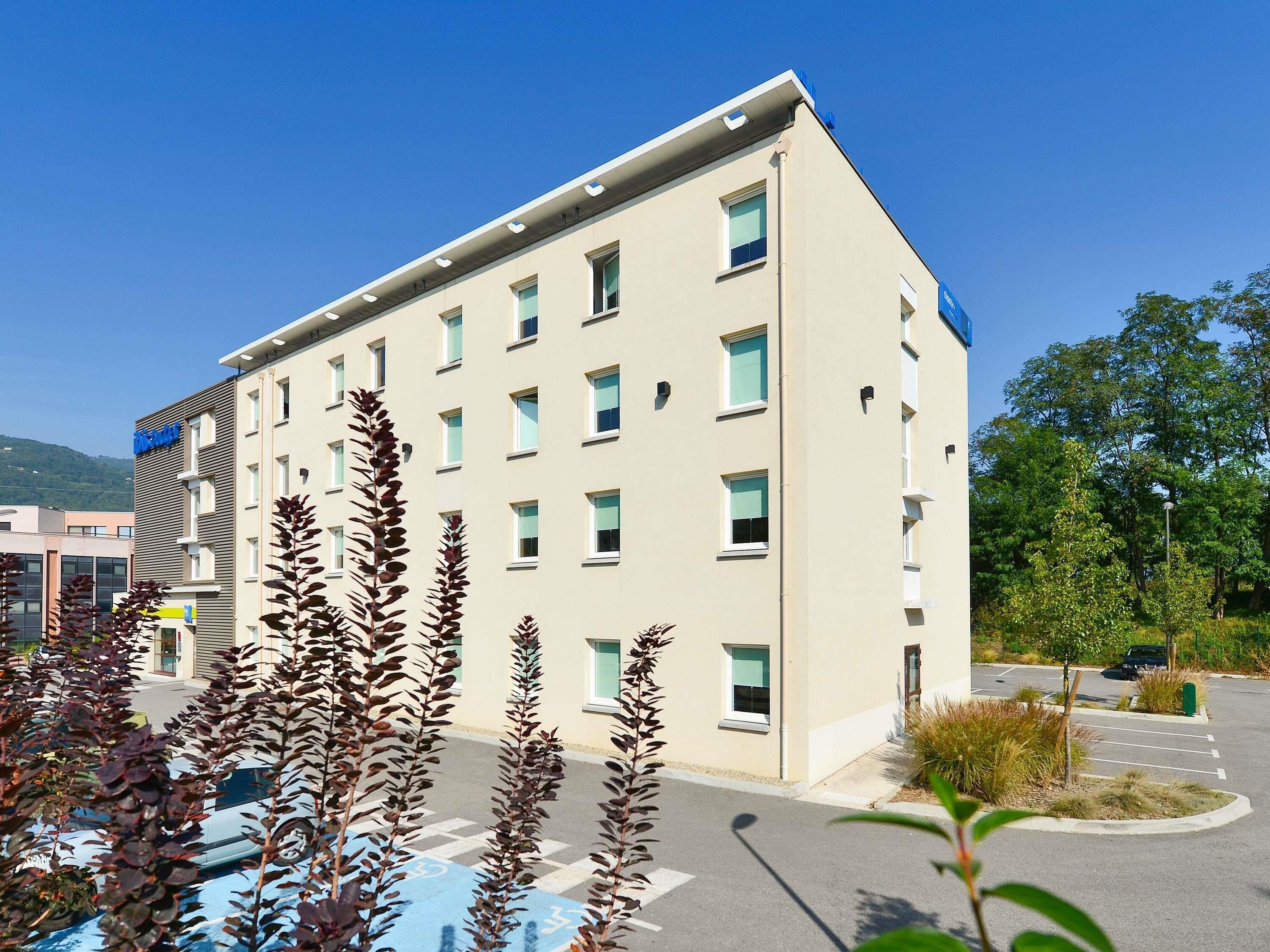 A multi-story hotel with a modern design, featuring a parking lot and surrounding greenery.