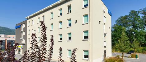 A multi-story hotel with a modern design, featuring a parking lot and surrounding greenery.