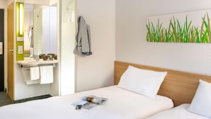 Une chambre d’hôtel comprenant un lit, une table de chevet, un miroir et une salle de bain avec un lavabo et un porte-serviettes.
