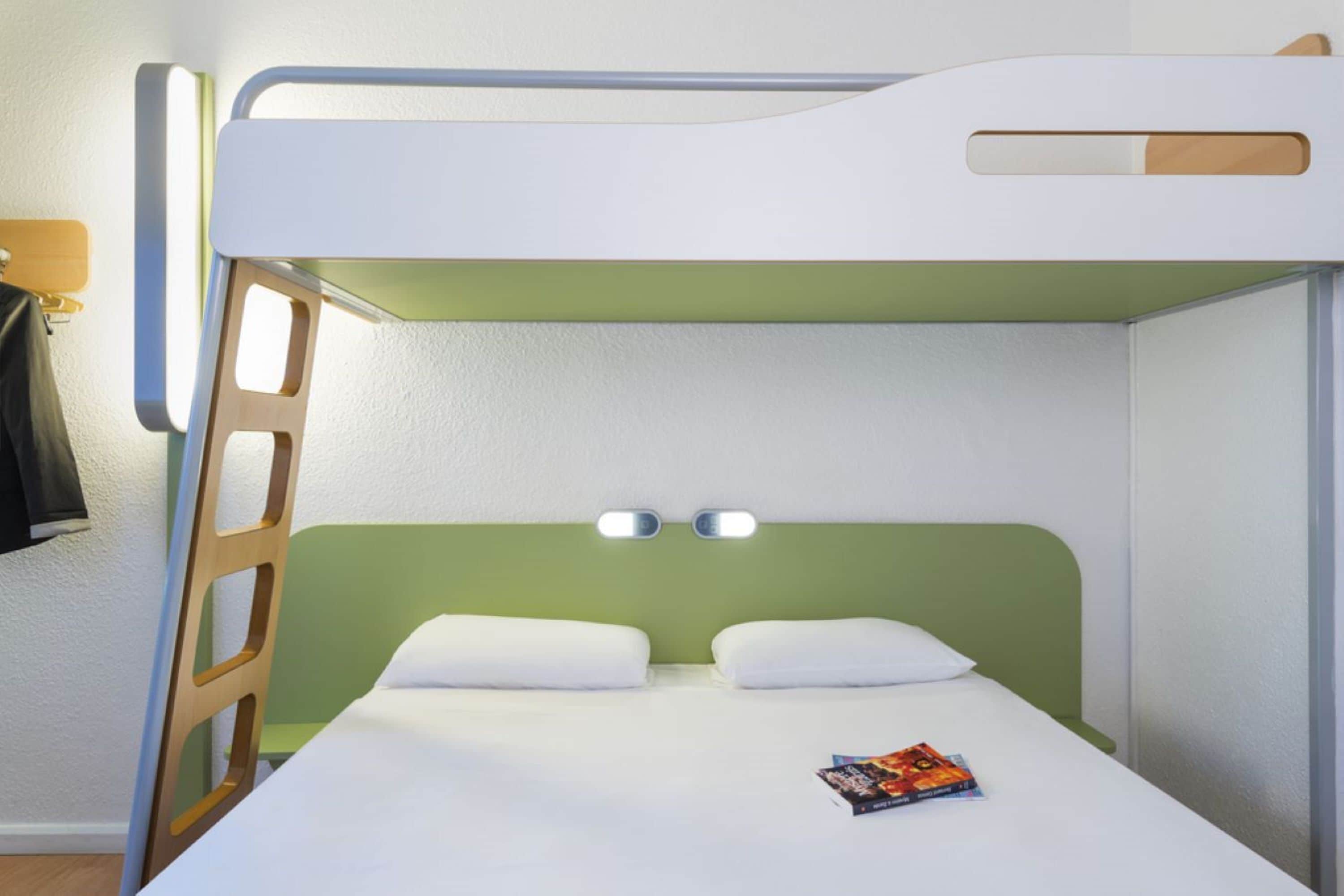 Una cama litera con cabecera verde, dos lámparas de noche y un libro en la cama inferior.