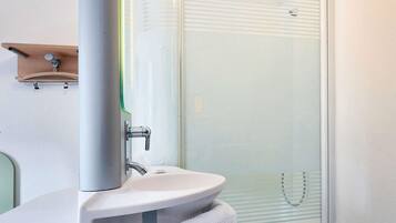 Une salle de bain moderne avec une douche à parois de verre, un lavabo blanc et une étagère en bois au-dessus du miroir.