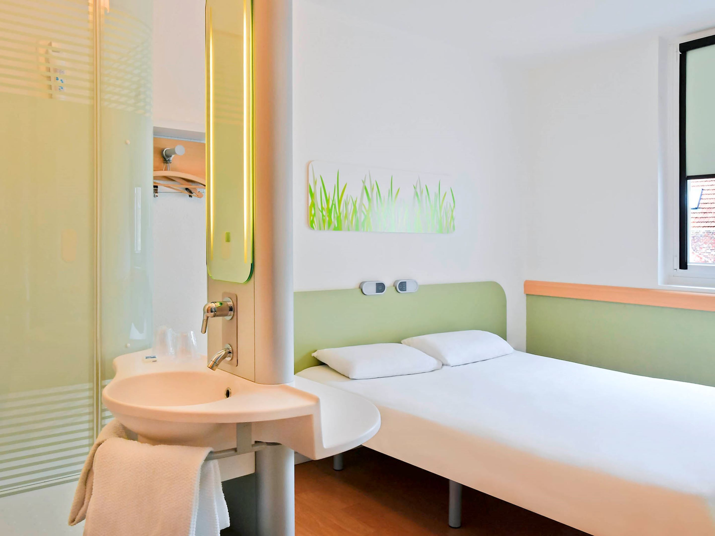 Una habitación de hotel con una cama individual, un lavamanos blanco y un espejo.