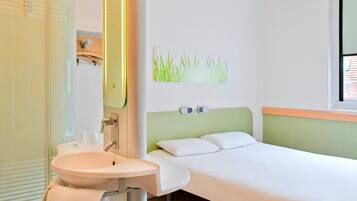 Una habitación de hotel con una cama individual, un lavamanos blanco y un espejo.