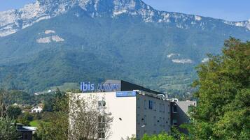 A building with 'ibis budget' signage, surrounded by greenery and mountains.