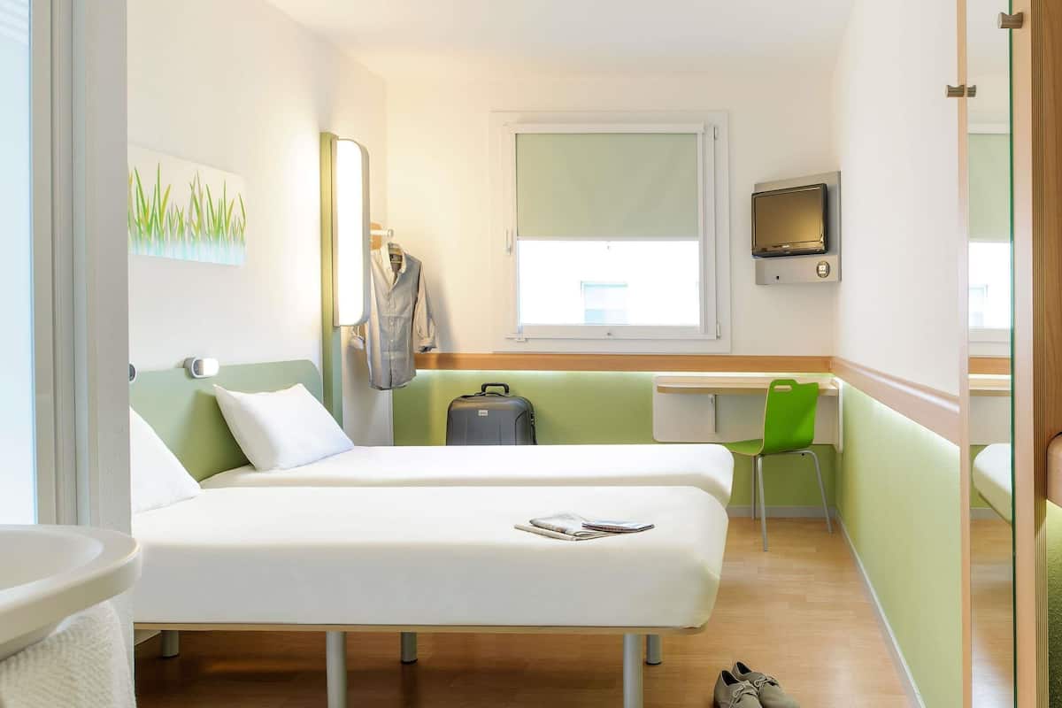 Habitación de hotel con dos camas, un escritorio, una silla, una maleta y un televisor.