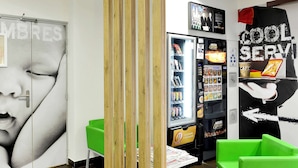 Un intérieur moderne avec un distributeur automatique, des sièges verts et un mur orné d’une image partielle d’un visage.