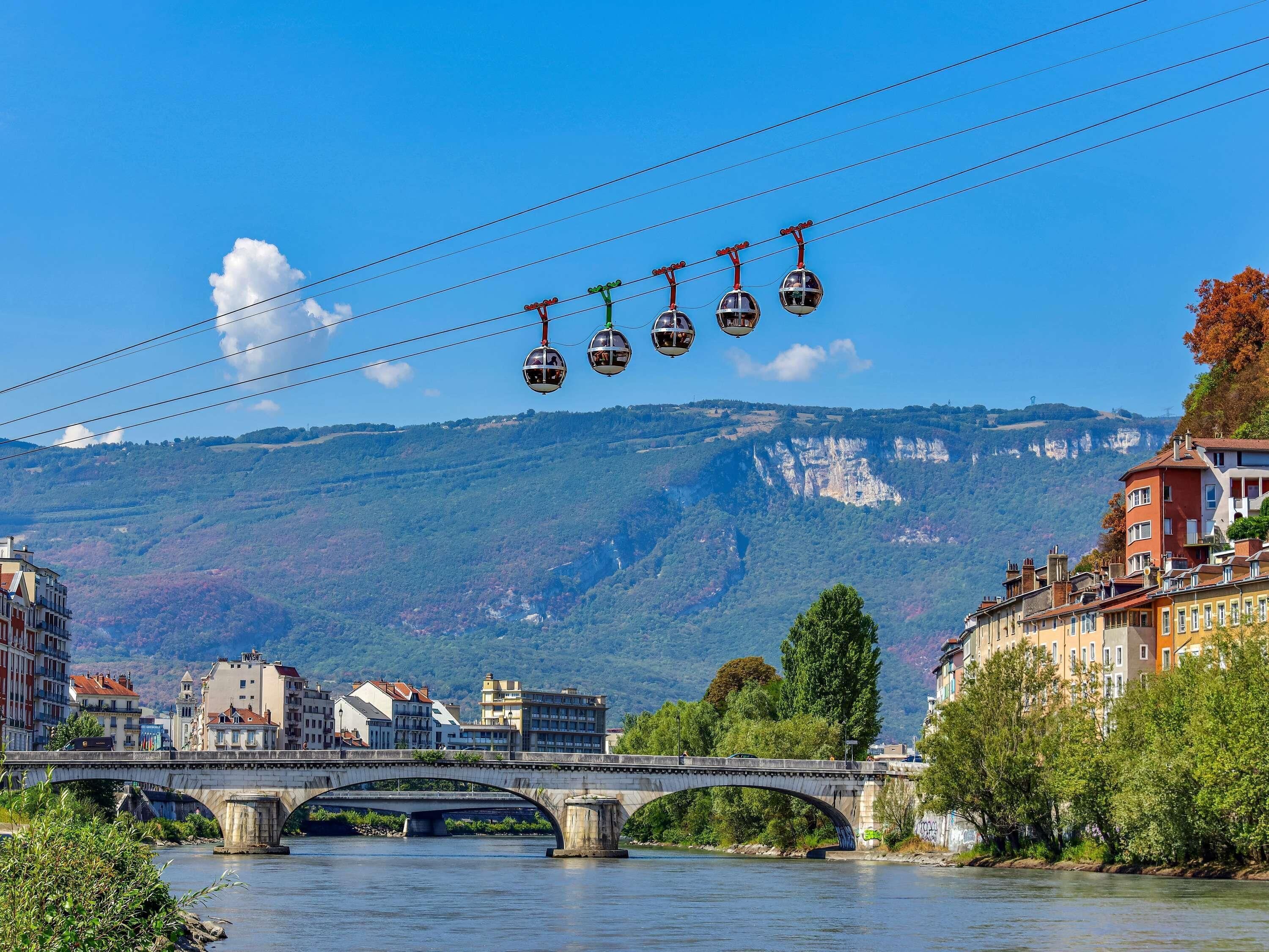 A bridge with a cable car system above it, a river below, and buildings on the riverbanks.