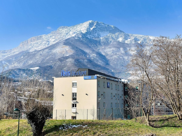 Un bâtiment sur lequel on peut lire l’inscription « ibis budget », avec une montagne enneigée en arrière-plan.
