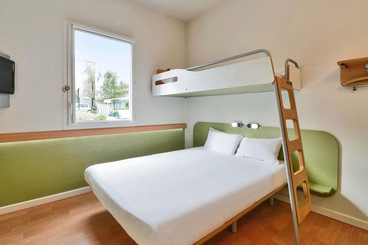 Una cama litera con escalera de madera, una ventana con vistas al exterior y un pequeño estante de madera en la pared.