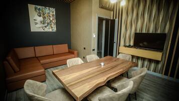 Una sala de estar moderna con una mesa de comedor de madera, sillas color beige, un sofá de cuero marrón, un televisor de pantalla plana montado en la pared y una cortina estampada.