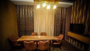 Een vergaderruimte met een grote houten tafel, zes gestoffeerde stoelen, een flatscreen televisie aan de muur en kamer met behang.