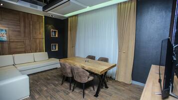 A modern living room with a wooden dining table, beige sofa, and a flat-screen TV.