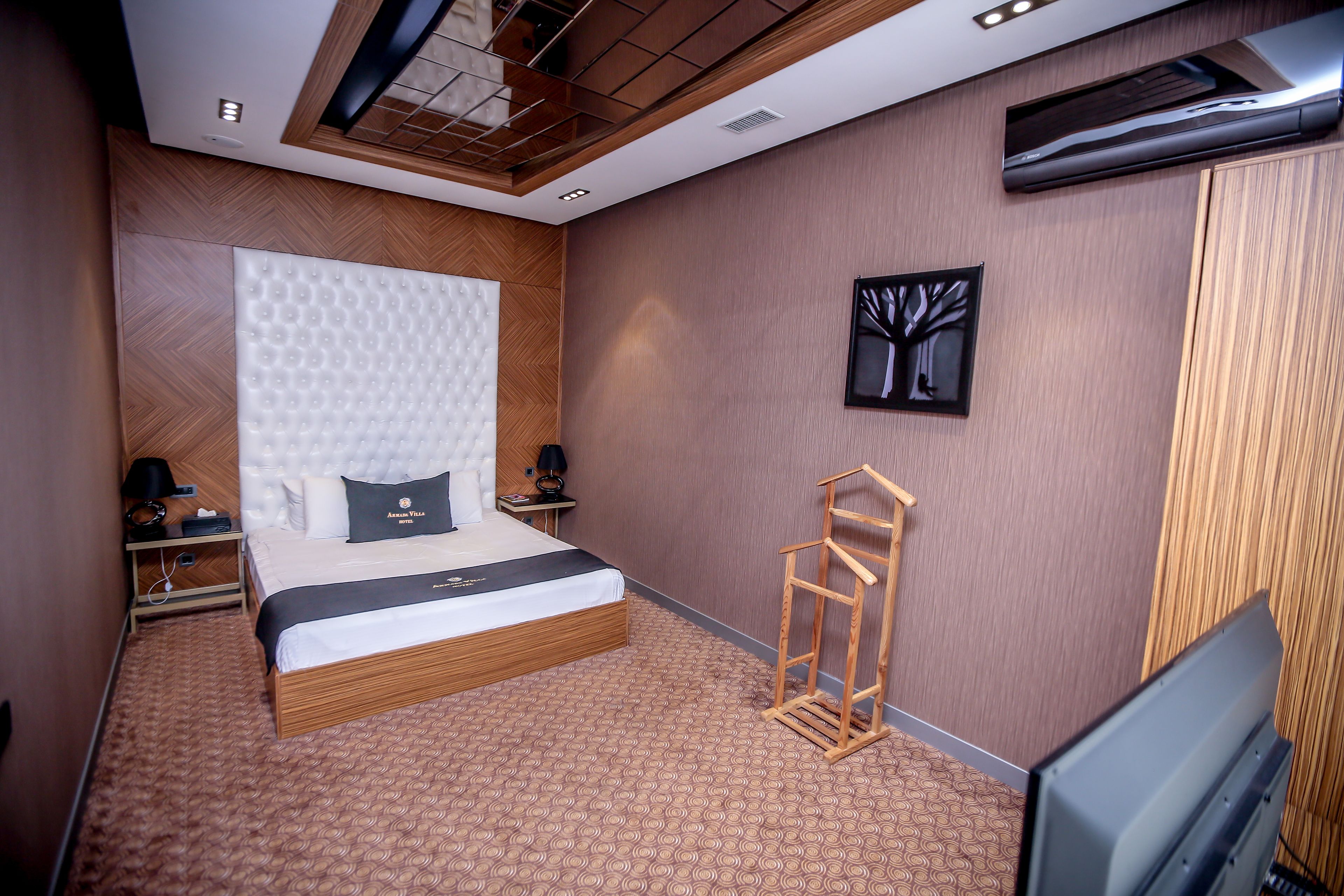 Una habitación de hotel moderna con una cama grande, un cabecero de madera, un televisor de pantalla plana y una obra de arte en la pared.