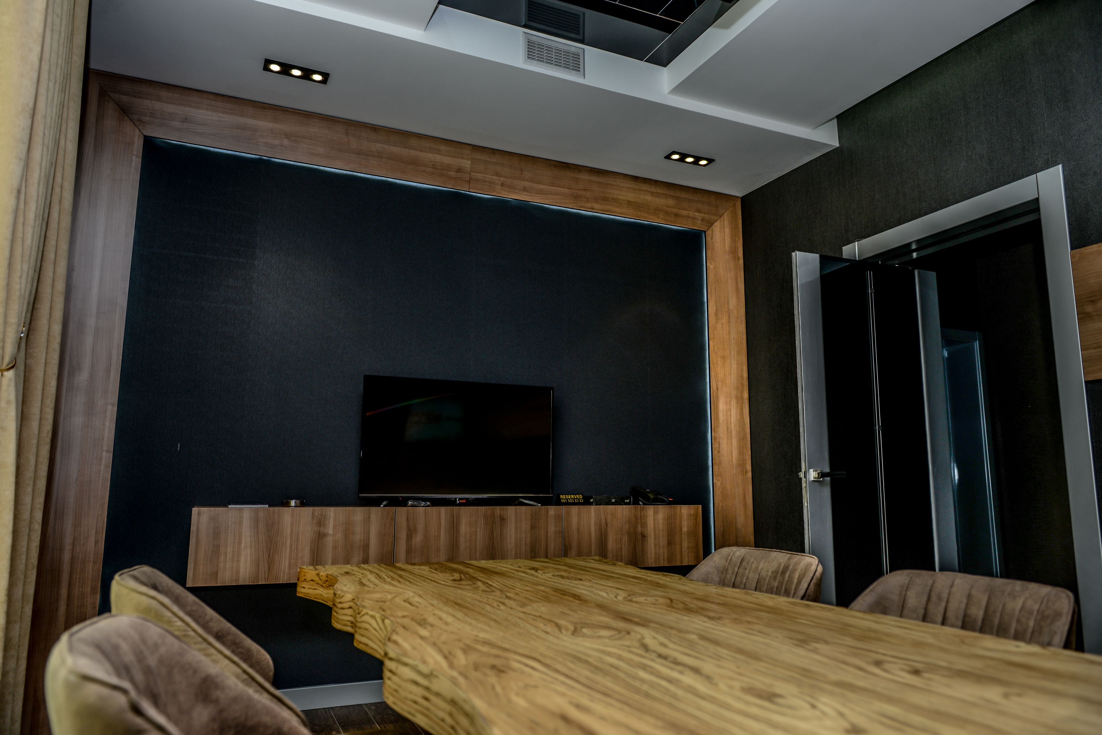 Una sala de estar moderna con una mesa de centro de madera, un televisor de pantalla plana montado en una pared oscura y una puerta a la derecha.