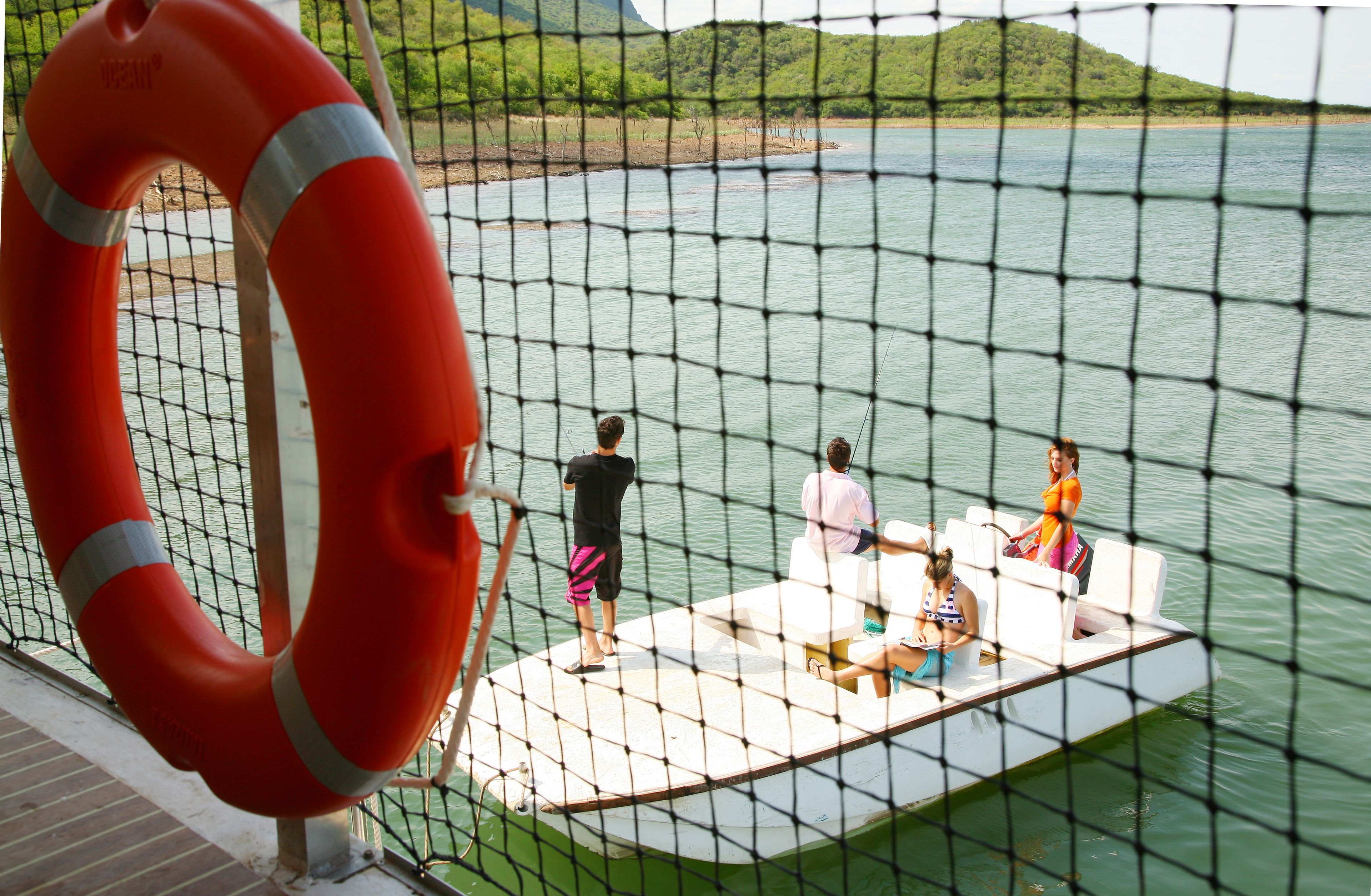 A boat with people on it, a lifebuoy, and a netted area.