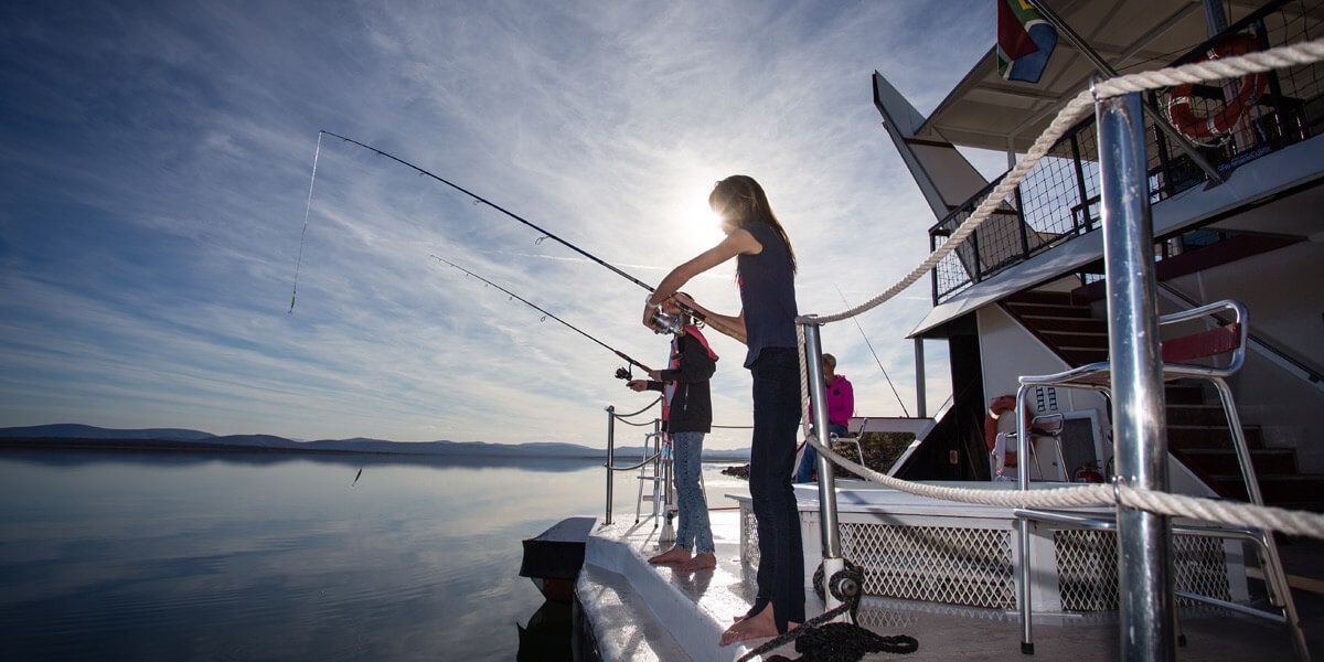 A boat with a person fishing, a railing, and a calm water body in the background.