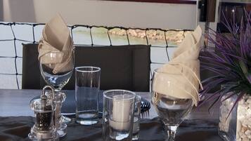 A dining table set with a white plate, cutlery, and clear glasses, with a scenic mountain view in the background.