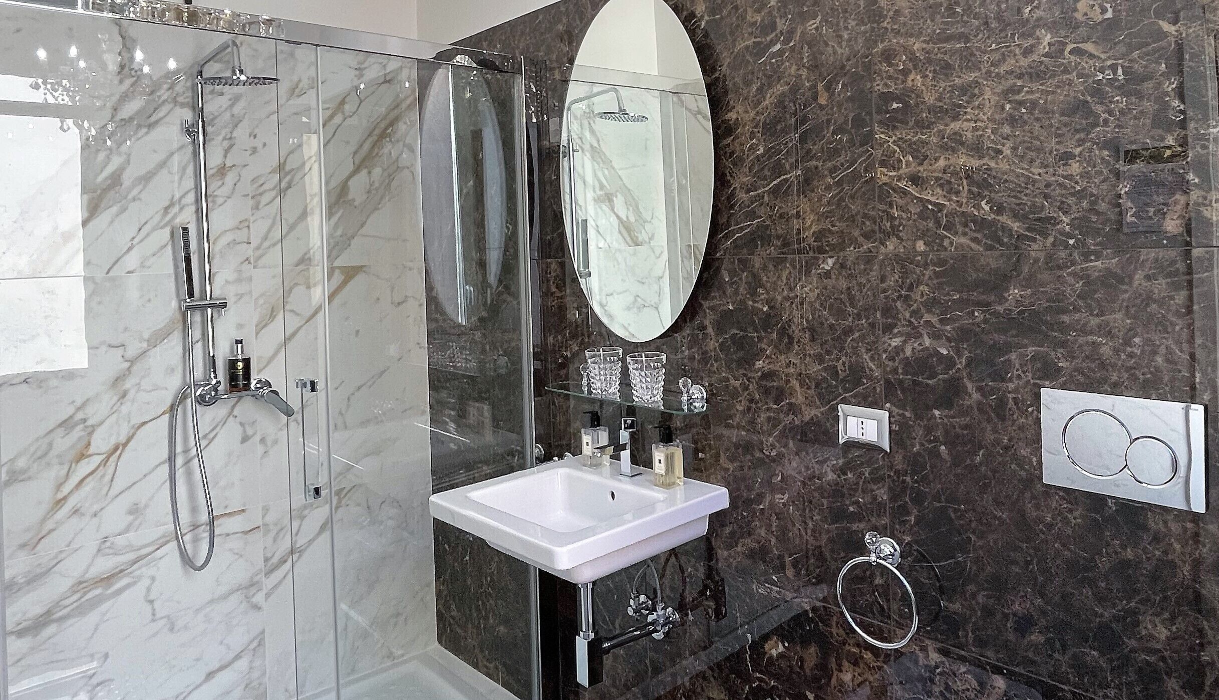 Ein modernes Badezimmer mit einer in Glas gefassten Dusche, einem weißen Waschbecken und einer Marmor-Spritzschutzwand.