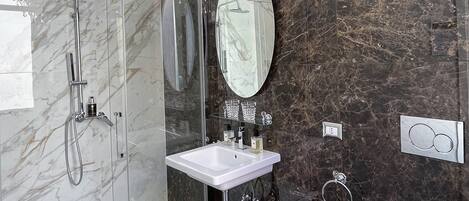 Ein modernes Badezimmer mit einer in Glas gefassten Dusche, einem weißen Waschbecken und einer Marmor-Spritzschutzwand.