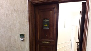 A wooden door with a plaque, a white vase with pink flowers, and a patterned doormat. - King Plaza (Rome)