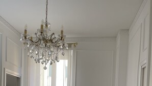A room with a wooden floor, a white chair with a leopard print cushion, a white table with gold trim, a chandelier, and a window with sheer curtains. - King Plaza (Rome)