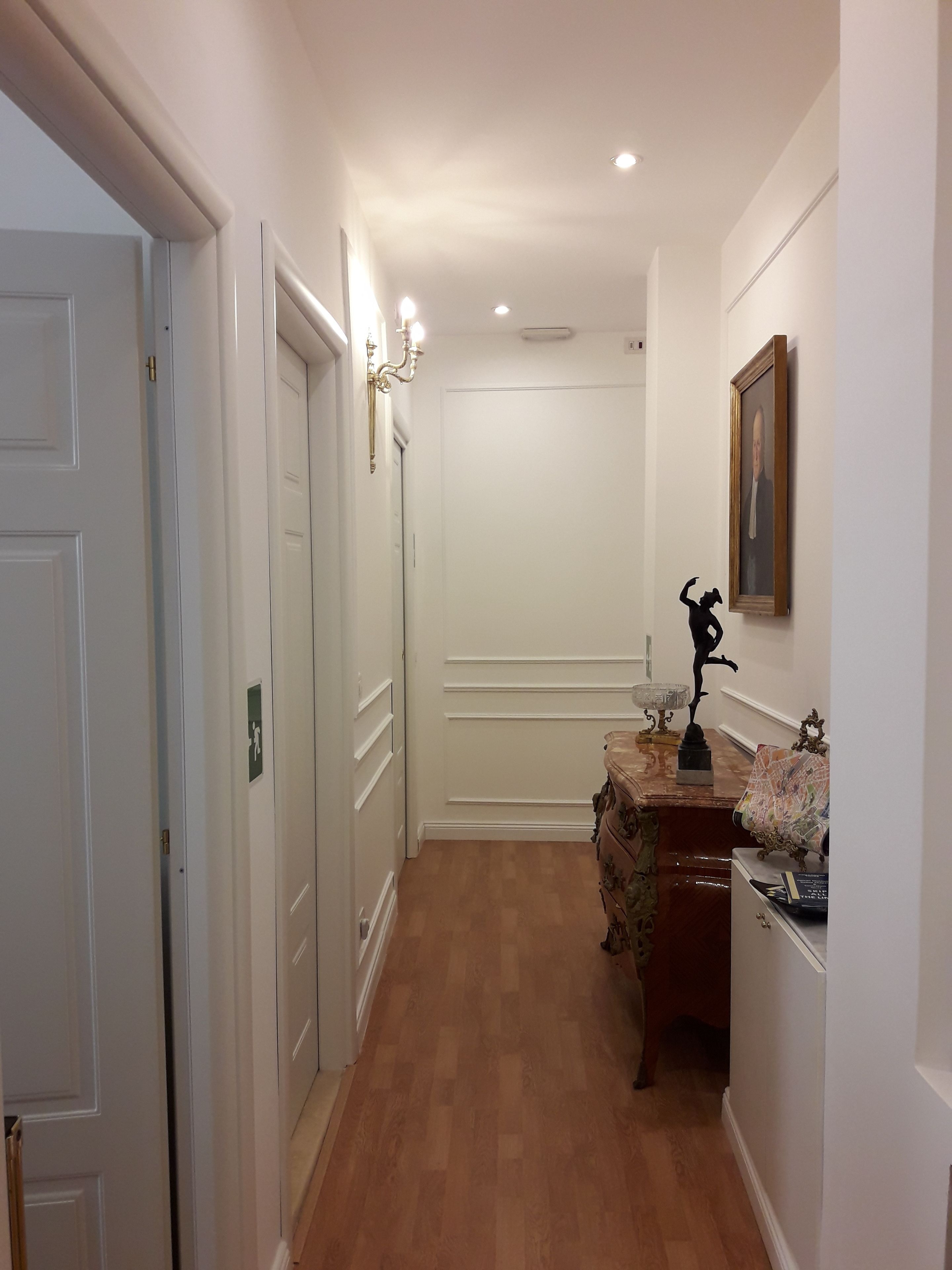 A hallway with wooden flooring, white walls, and a marble-topped console table with a statue.