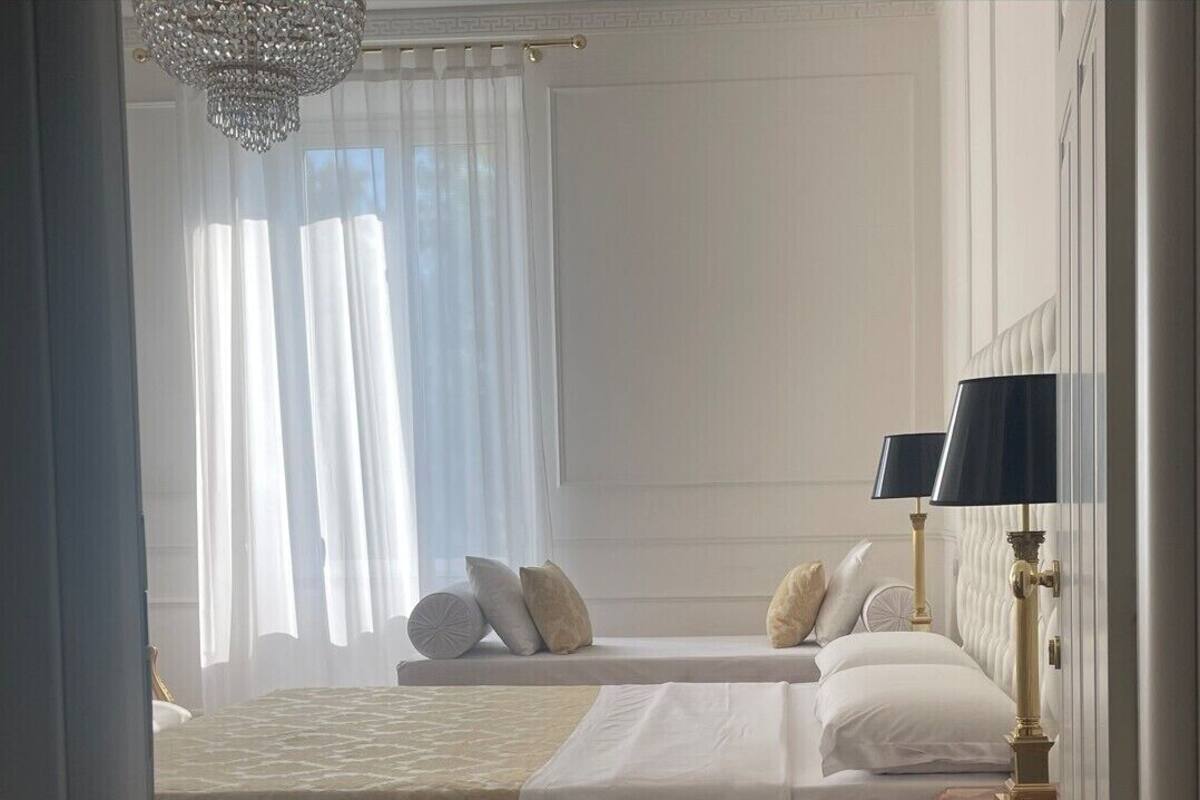 A hotel room with two beds, a chandelier, and a nightstand with a lamp.