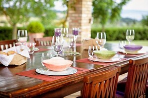 A dining table set outdoors with multiple chairs, wine glasses, and bowls.