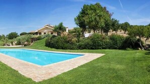 A swimming pool surrounded by well-maintained grass and a house in the background. - La Cavetta Country House (Trevignano Romano)