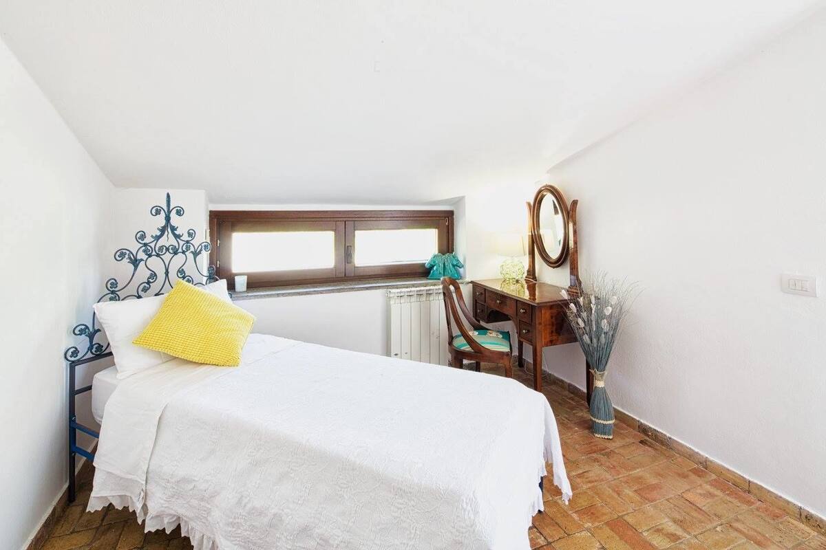 Een slaapkamer met een bed, een dressoir, een stoel, een spiegel en een raam.