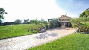 A house with a paved driveway leading to a covered entrance, surrounded by well-maintained lawns and trees. - La Cavetta Country House (Trevignano Romano)