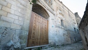 A stone building with a large wooden door and an arched window. - Giardini di Pietra (Matera)