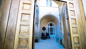 An open wooden door leading to a courtyard with a stone bench, a wreath, and a window with a white frame. - Giardini di Pietra (Matera)