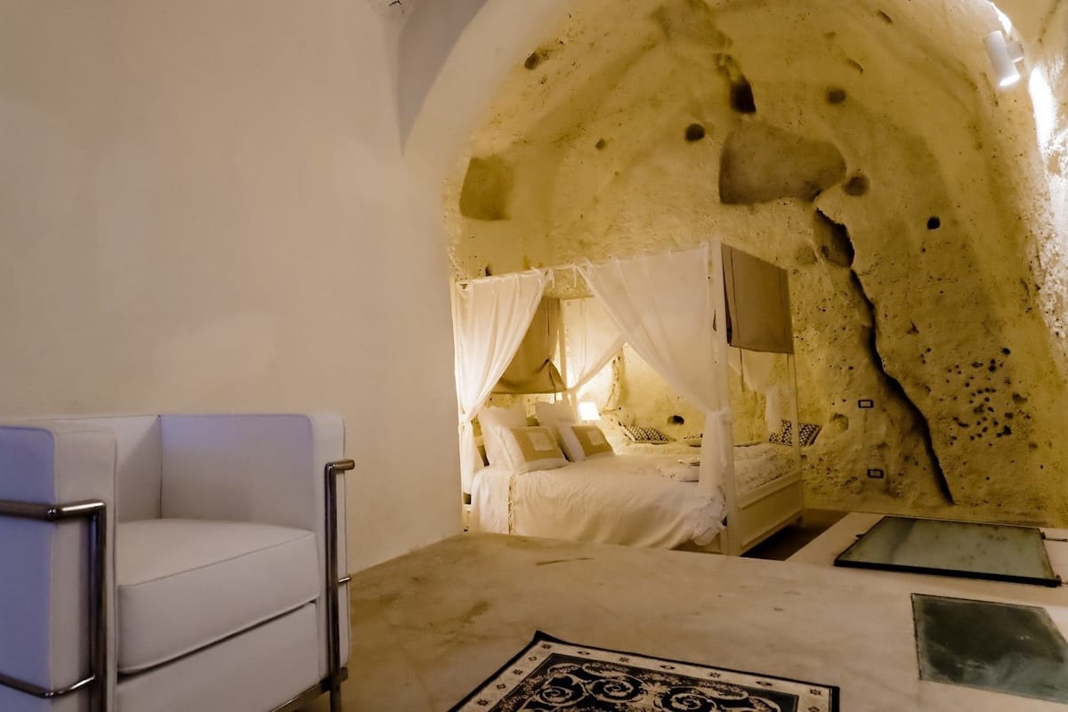 A room with a white cushioned chair, a bed with a canopy, and a unique cave-like interior.