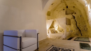 A room with a white cushioned chair, a bed with a canopy, and a unique cave-like interior. - Giardini di Pietra (Matera)