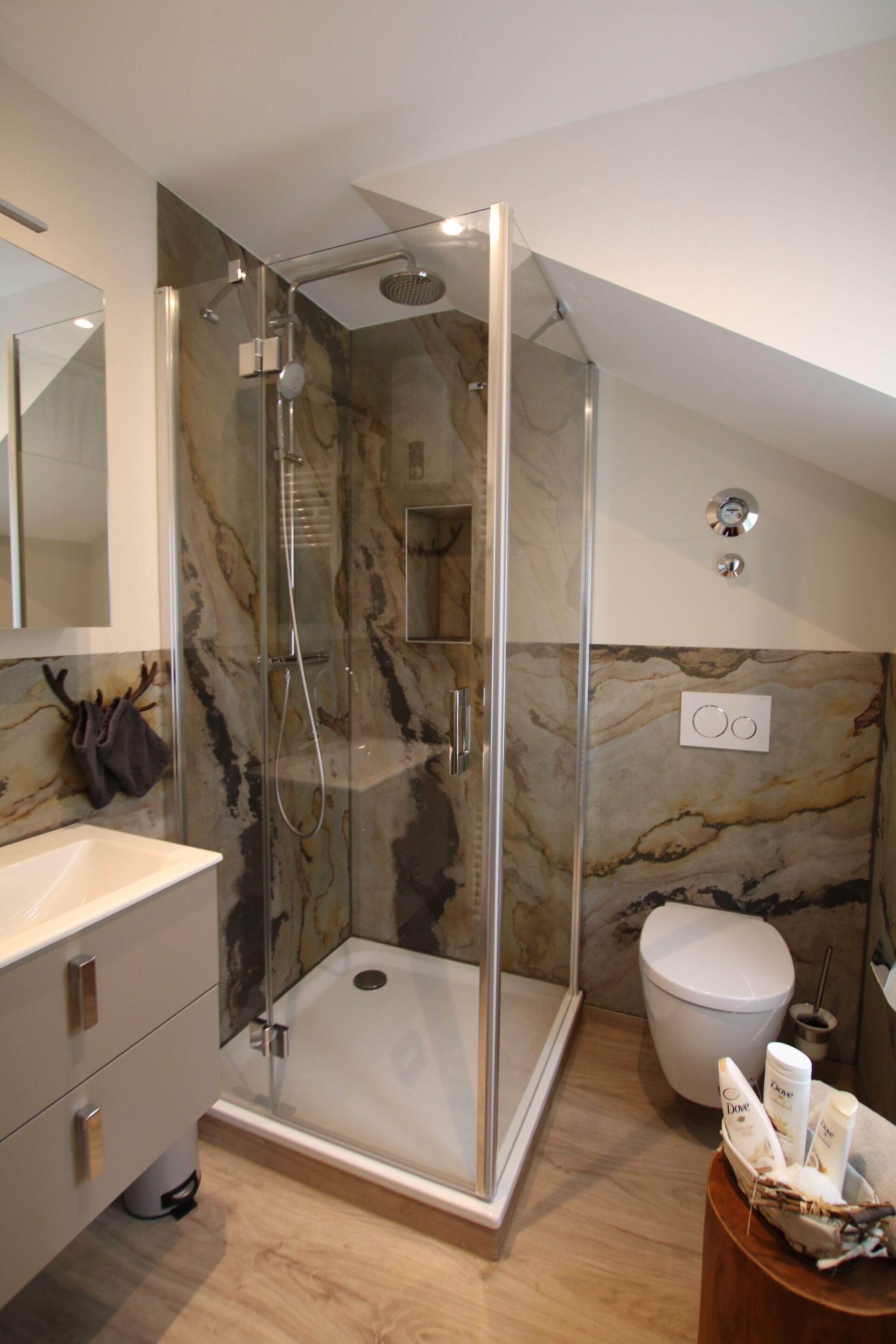 A modern bathroom with a glass-enclosed shower, a marble wall, a white sink, and a toilet.