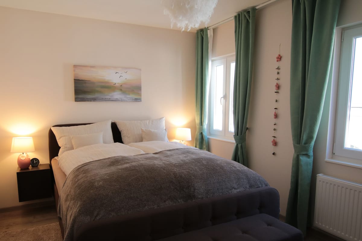 Quarto com cama, luminárias de cabeceira, um quadro e cortinas.