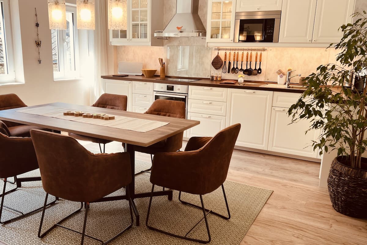 Cozinha moderna com armários brancos, uma ilha central e um espaço de jantar com mesa de madeira e cadeiras marrons.