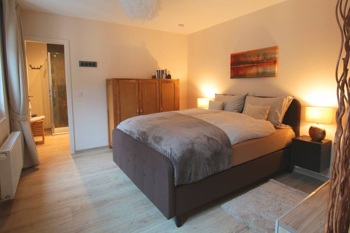 Quarto com cama grande, guarda-roupa de madeira, abajures e um quadro na parede.