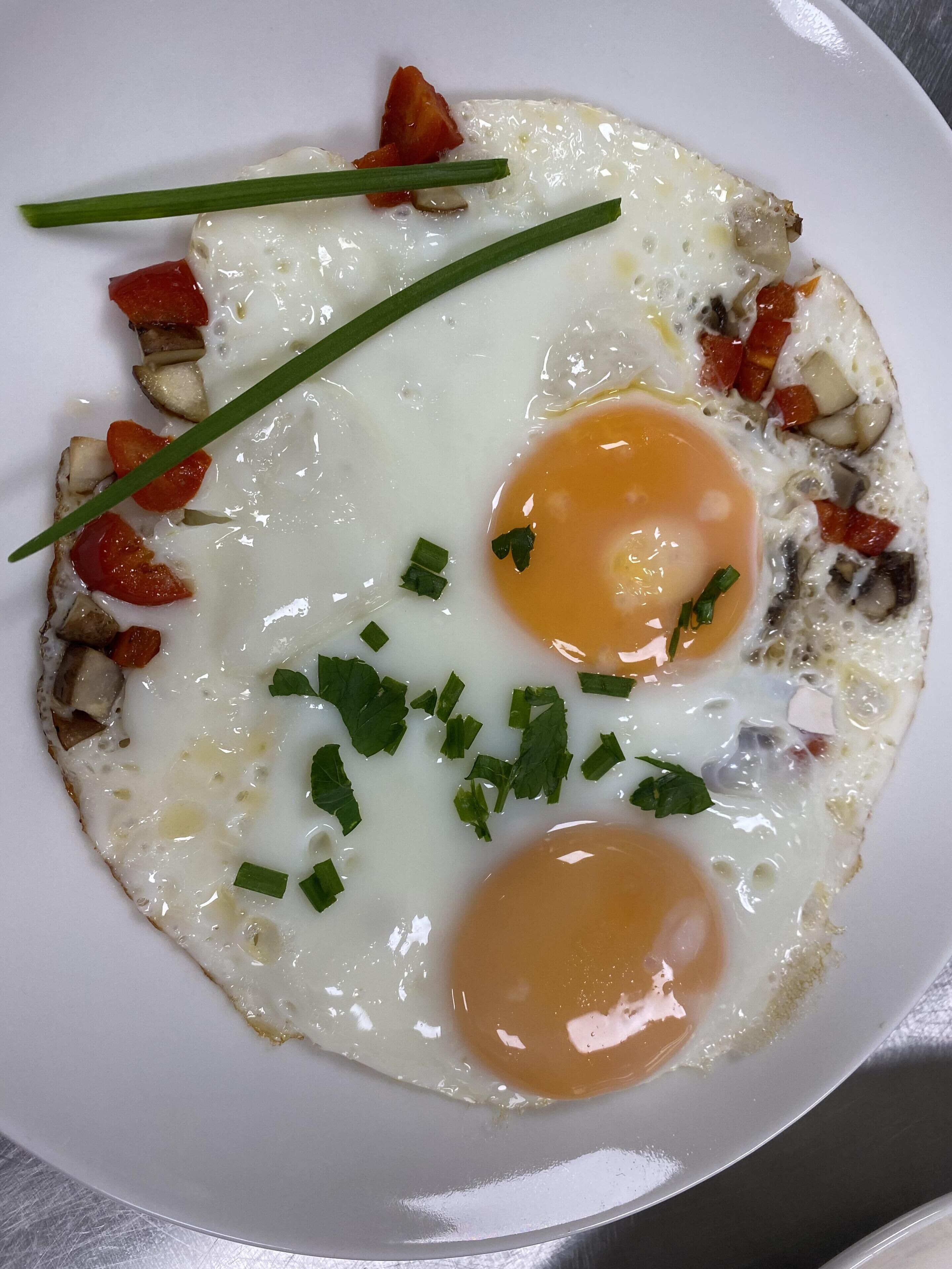 A plate with two sunny-side-up eggs, diced tomatoes, and chopped green onions.