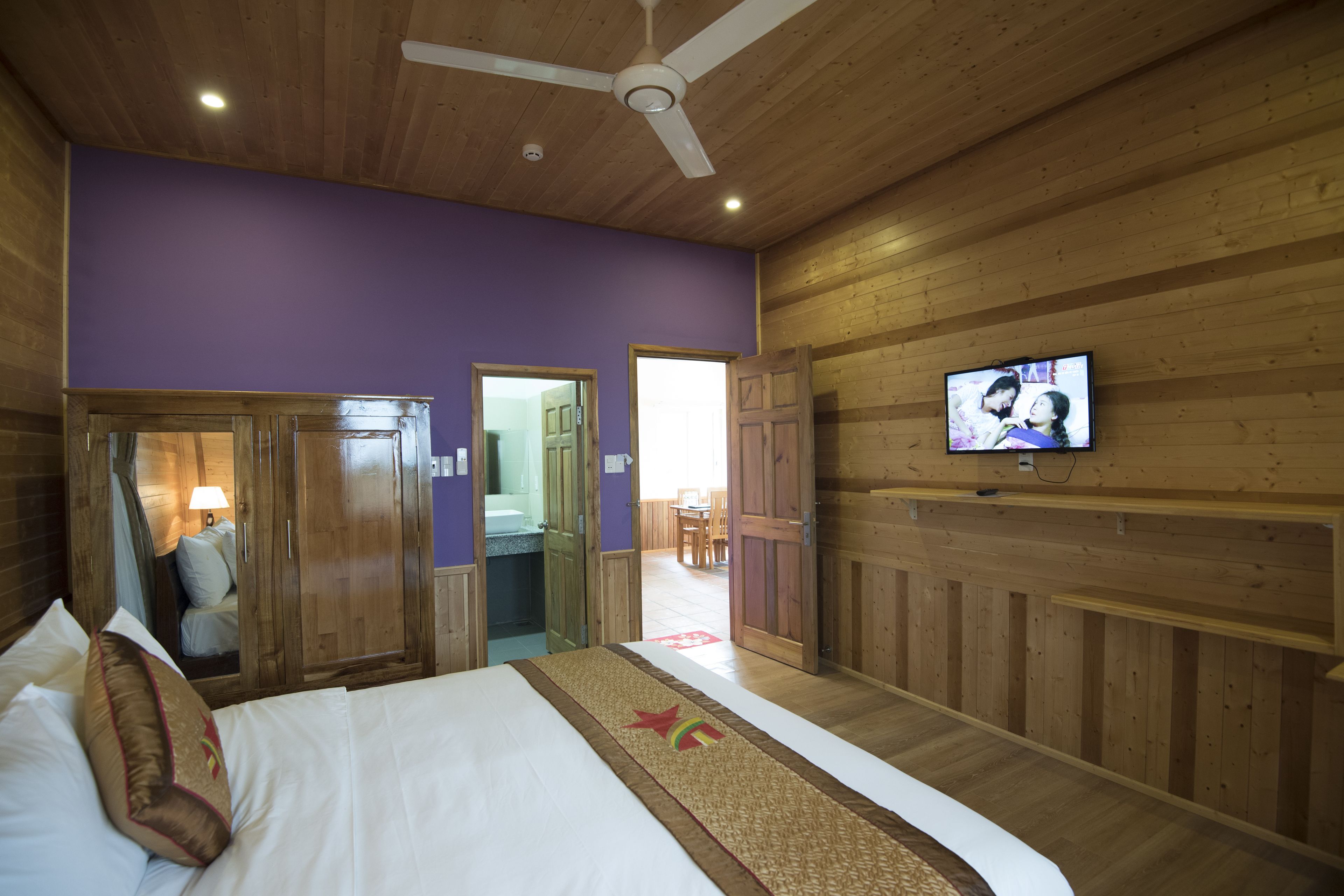 Un dormitorio con cama, paredes de madera, ventilador de techo y televisión en la pared.