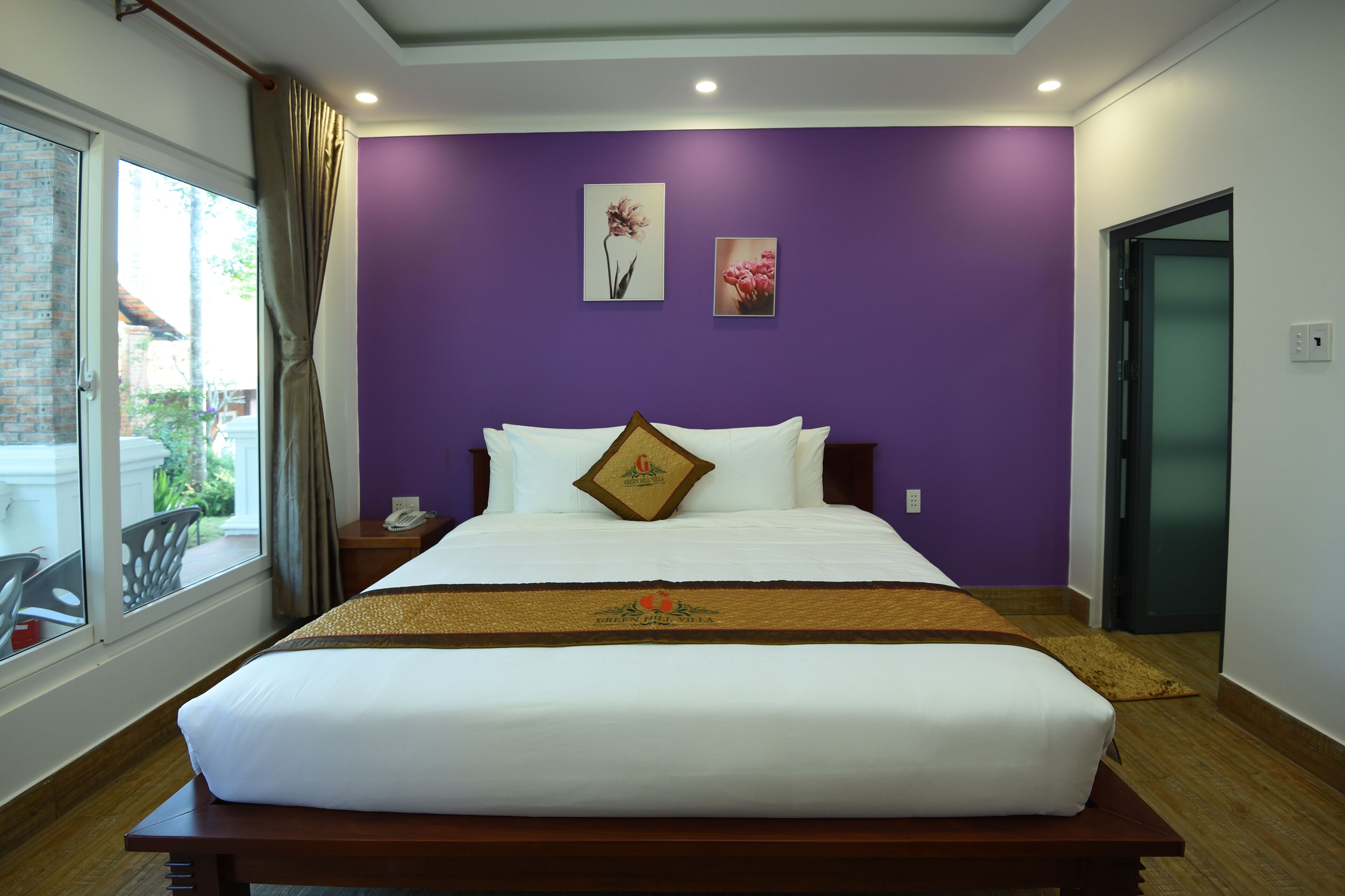 Habitación de hotel con una cama grande, paredes moradas y una ventana con cortinas.