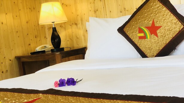 A neatly made bed with a white sheet, a decorative pillow with a red star and a rainbow, and a small bouquet of purple flowers. - Doi Sao Phu Quoc (Phu Quoc)