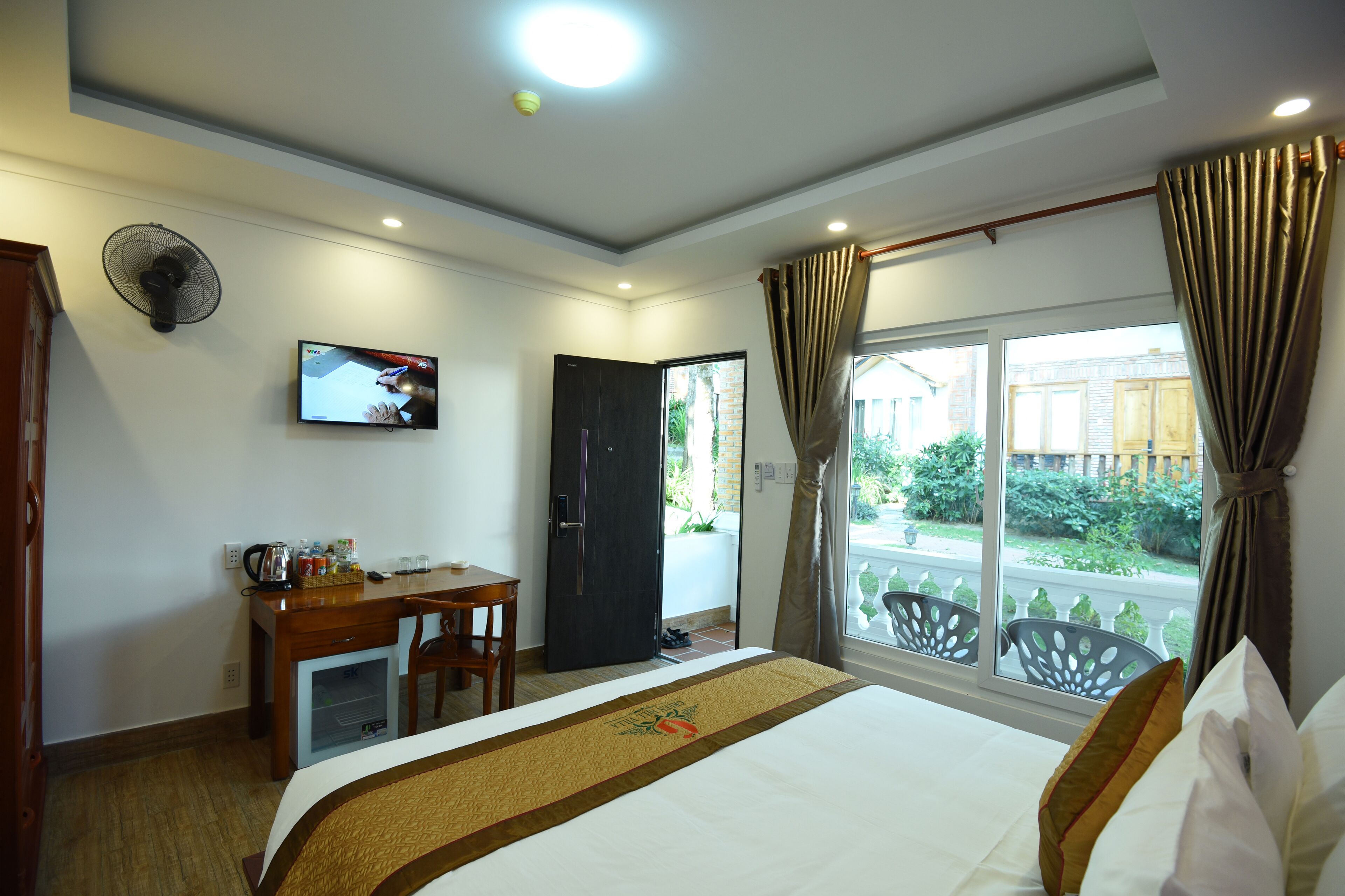 A hotel room with a bed, a desk with a chair, a television, and a window with curtains.