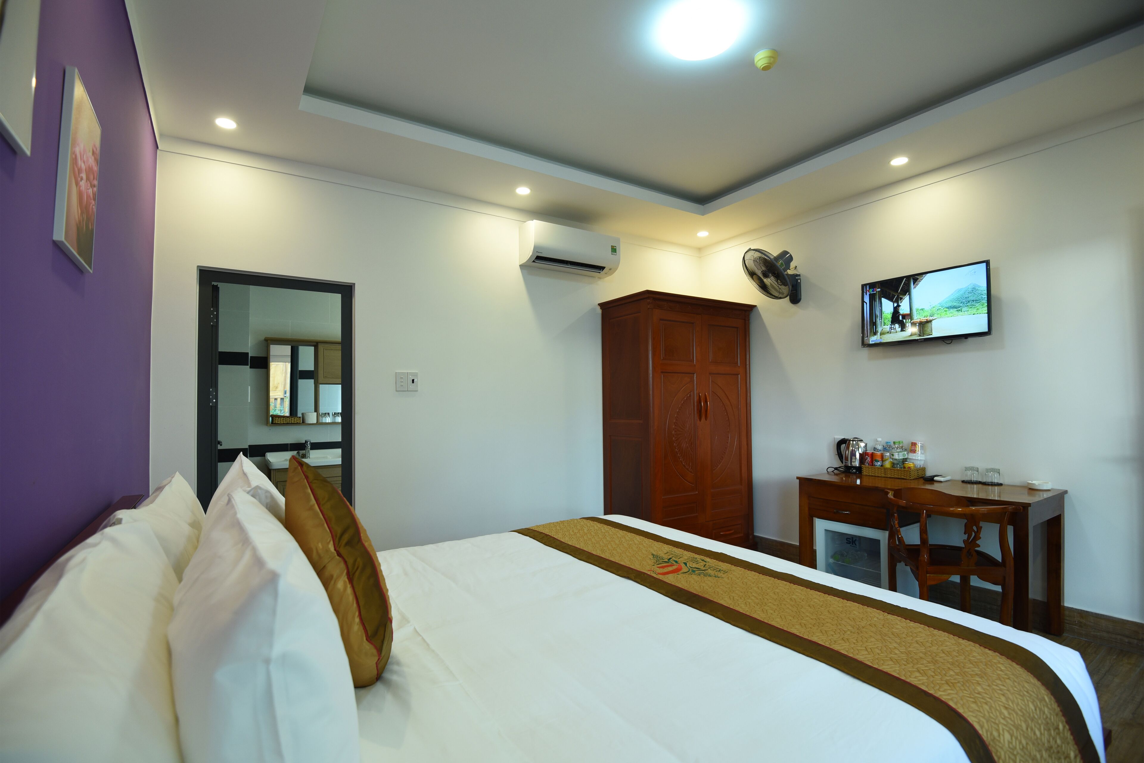 Una habitación de hotel con cama, escritorio, televisión y aire acondicionado.