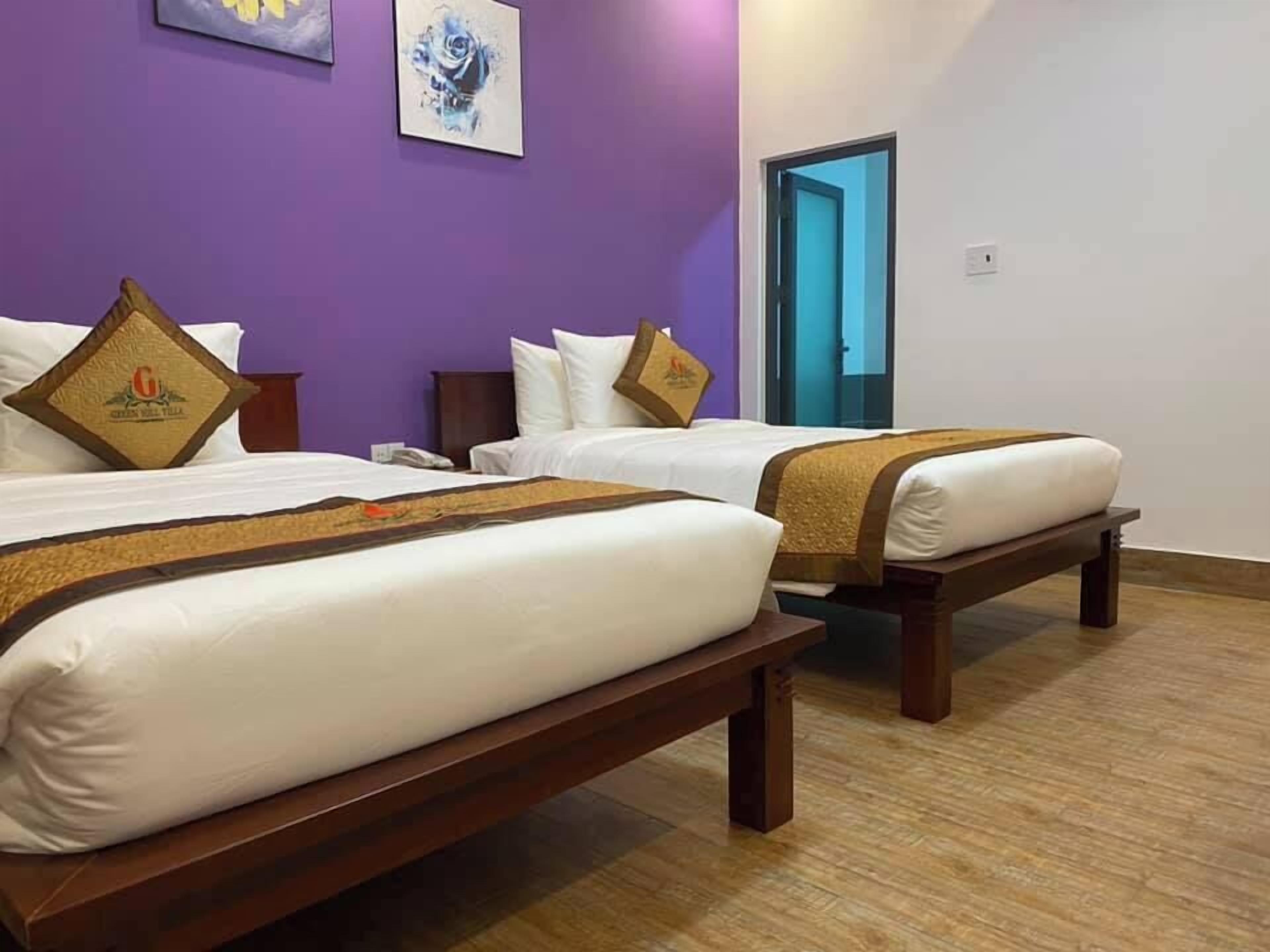 A hotel room with two beds, a purple wall, and a door with a blue frame.